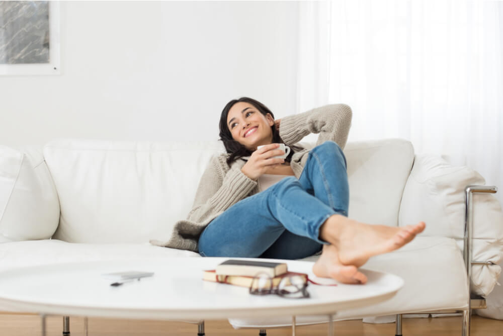 A woman smiling and relaxing on sofa at home with a coffee in hand