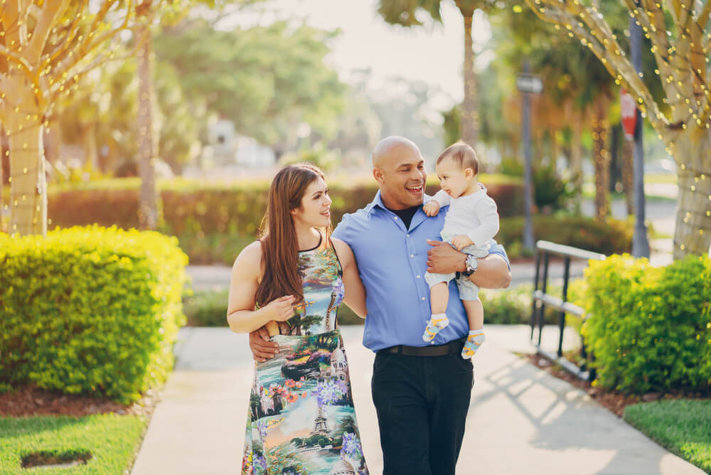 Two parents with young child walking outside among trees and greenery