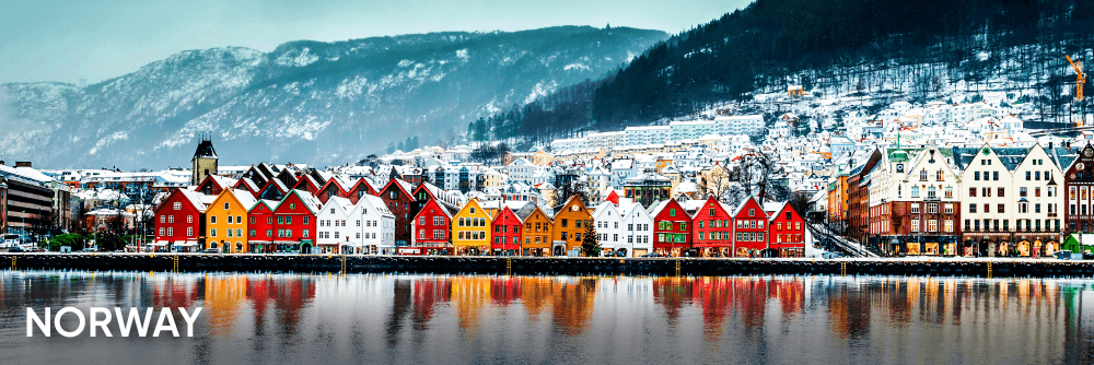a view of white, red, yellow and orange Norwegian buildings by the water with snowy mountains behind